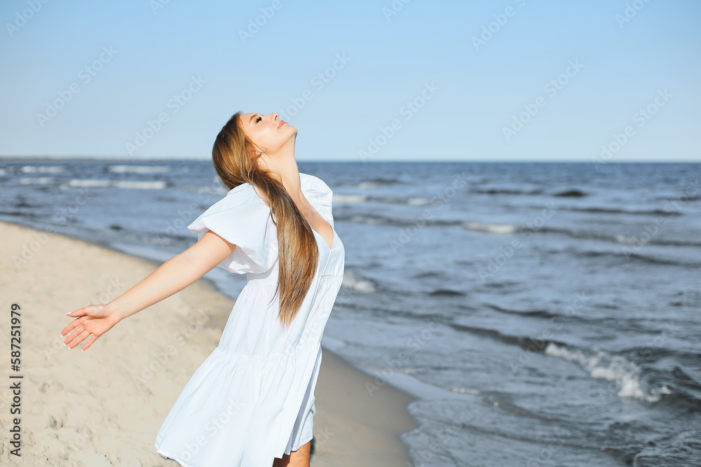 Happy, beautiful woman on the ocean beach standing in a white summer dress, open arms Happy, beautiful woman on the ocean beach standing in a white summer dress, open arms