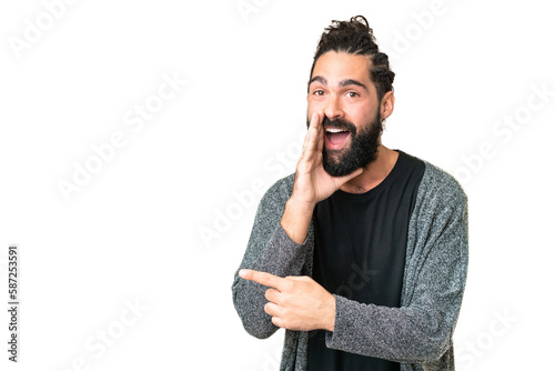 Young man with beard over isolated chroma key background pointing to the side to present a product and whispering something photo