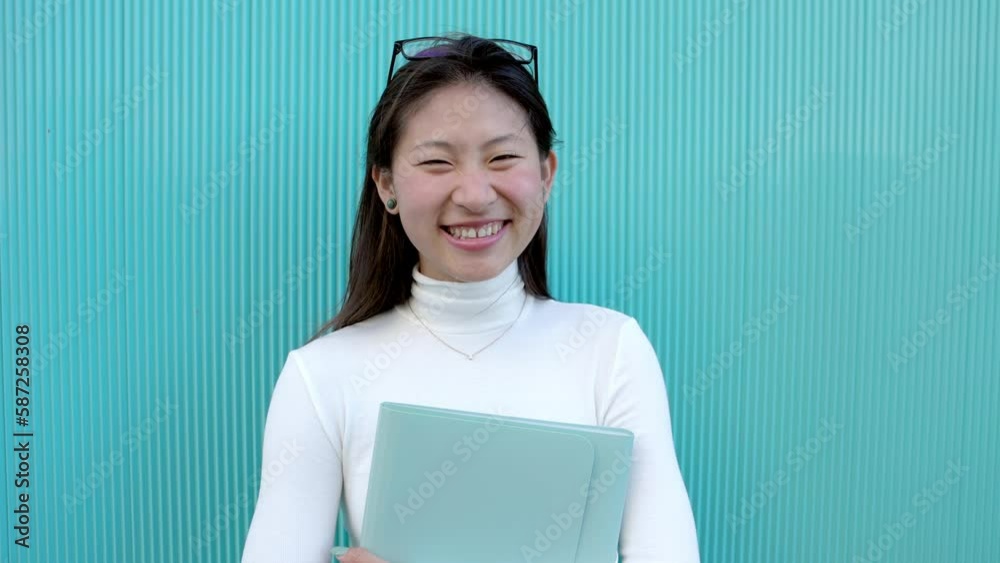 Happy female asian student smiling at camera standing over aquamarine building college wall background Happy female asian student smiling at camera standing over aquamarine building college wall background