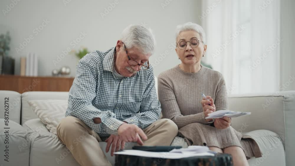 Worried senior retired couple checking calculating bills sitting on couch at home. Do paperwork discuss unpaid debt taxes, stressed family. Financial difficulties, money problem in elderly age concept