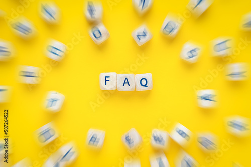 FAQ - frequently asked questions as text on wooden cubed with movemend effect of other cubes with yellow background photo