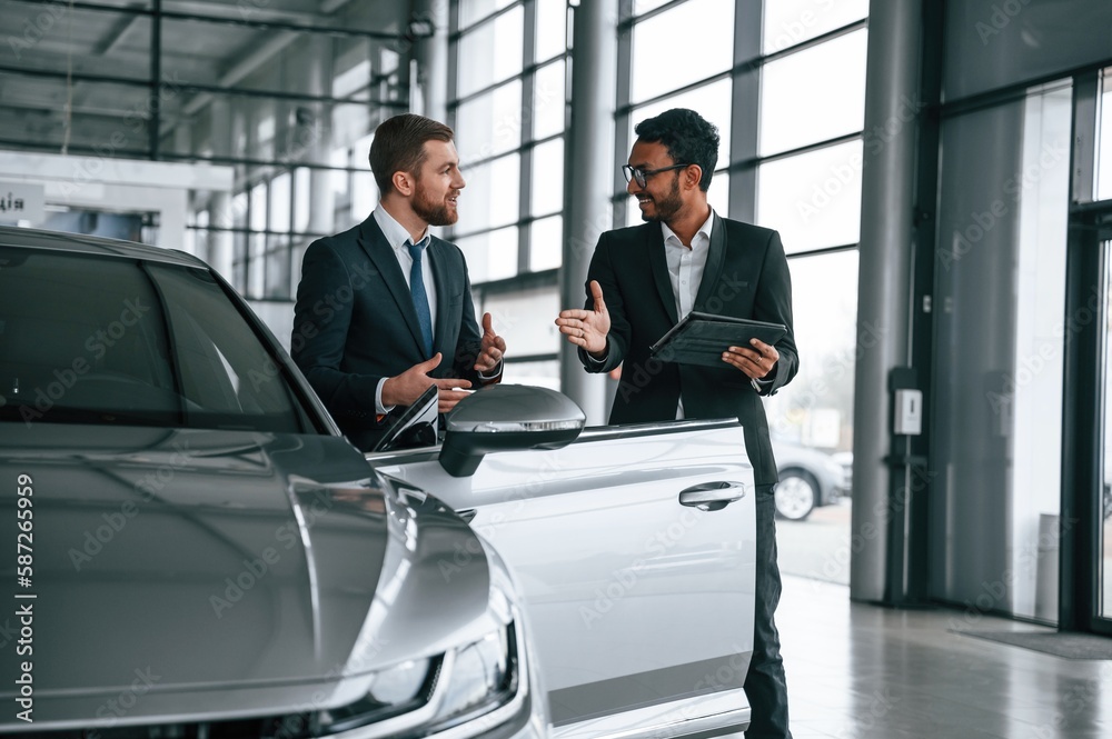 Standing and talking near automobile. Man is consulting the customer in the car showroom Standing and talking near automobile. Man is consulting the customer in the car showroom