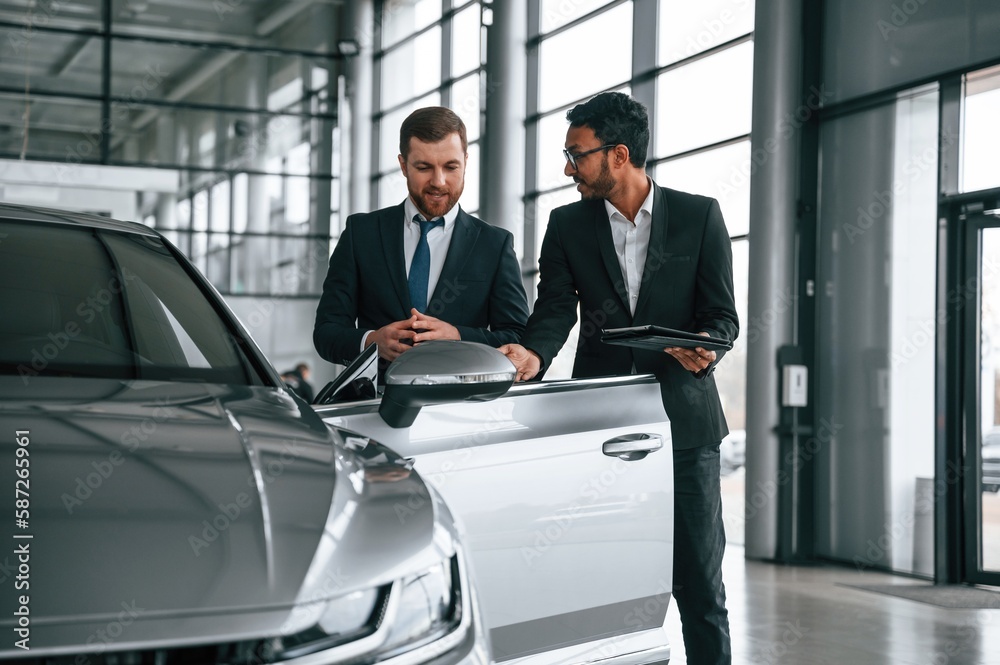 Checking quality of the vehicle. Man is consulting the customer in the car showroom Checking quality of the vehicle. Man is consulting the customer in the car showroom