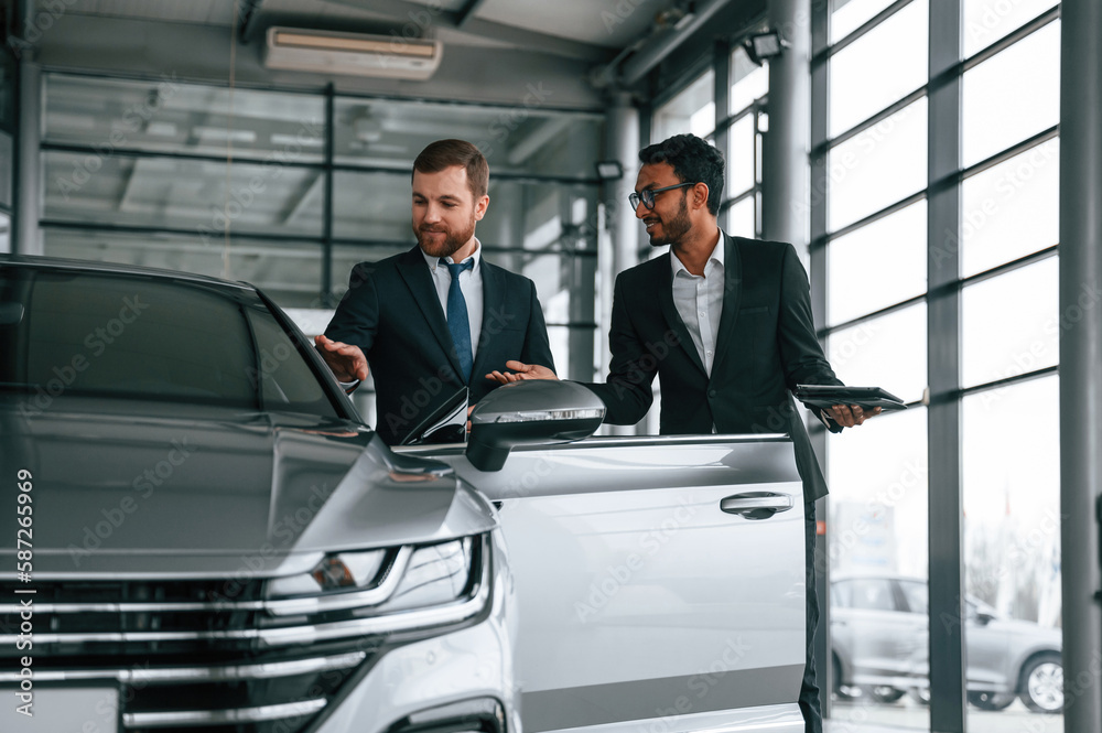 Standing and talking near automobile. Man is consulting the customer in the car showroom Standing and talking near automobile. Man is consulting the customer in the car showroom