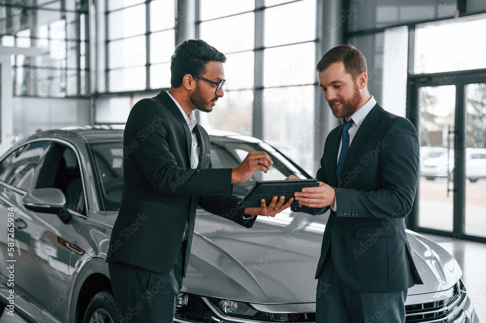 Using graphic tablet. Man is consulting the customer in the car showroom Using graphic tablet. Man is consulting the customer in the car showroom
