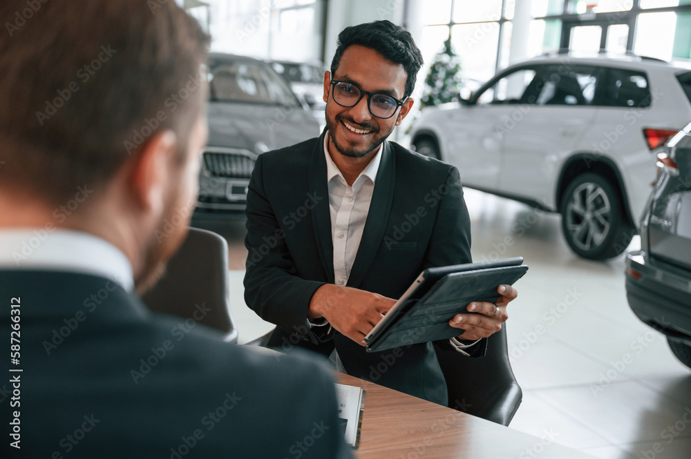 Using graphic tablet. Man is consulting the customer in the car showroom Using graphic tablet. Man is consulting the customer in the car showroom