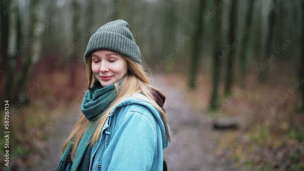 Girl traveler walks in forest or park in autumn clothes against trees, looks at camera and toothy smile. Portrait of happy female enjoy hike in nature outdoors. Beautiful model posing alone. Girl traveler walks in forest or park in autumn clothes against trees, looks at camera and toothy smile. Portrait of happy female enjoy hike in nature outdoors. Beautiful model posing alone.