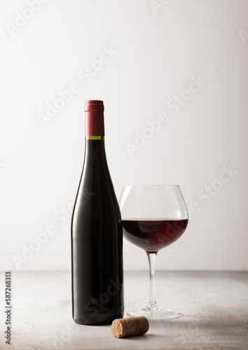 Bottle and glass of red wine with cork on light background.