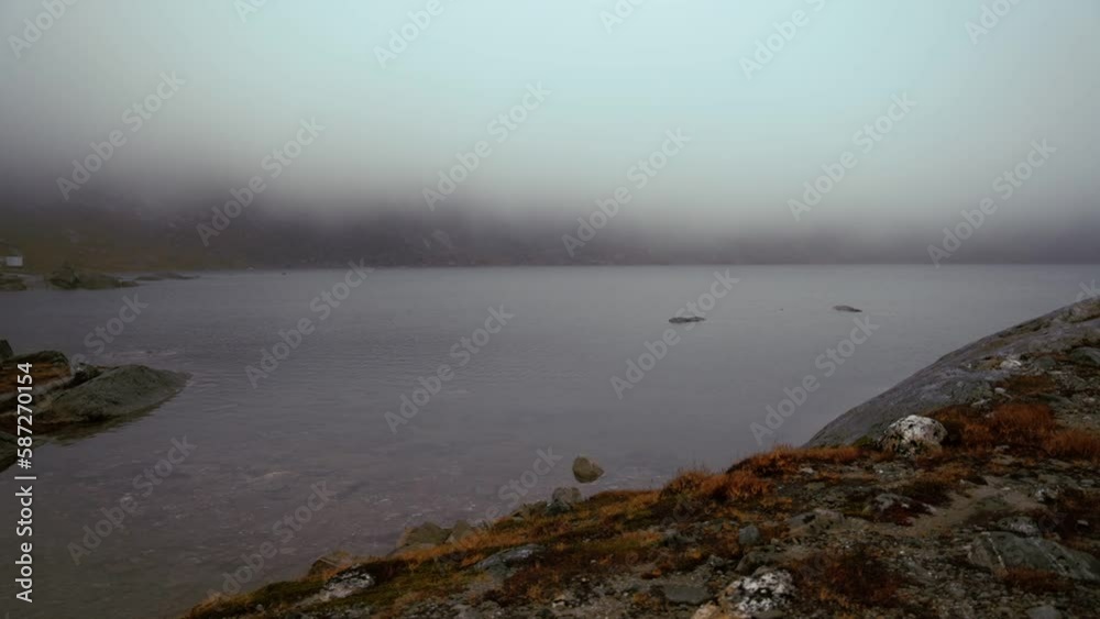 Wide shot overlooking the mountain lake as the foggy clouds take over. Panning right Wide shot overlooking the mountain lake as the foggy clouds take over. Panning right
