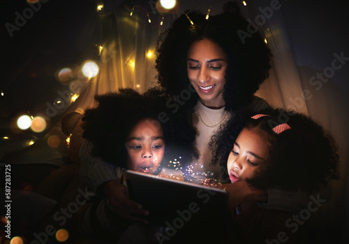Tablet, night a mother reading to her kids in a tent while camping in the bedroom of their home together. Black family, story or children with a woman storytelling to her kids at bedtime for bonding photo