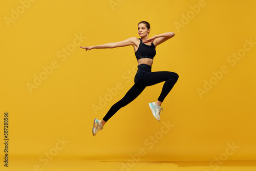 Dynamic image of young beautiful girl in sportswear training, running against yellow studio background. Cardio session. Concept of sport, healthy and active lifestyle, beauty, fitness