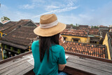 Female tourist in hat backpacking, Hoi An, Vietnam, sitting and drinking hot tea for breakfast, overlooking the old city rooftop in the coffee shop.