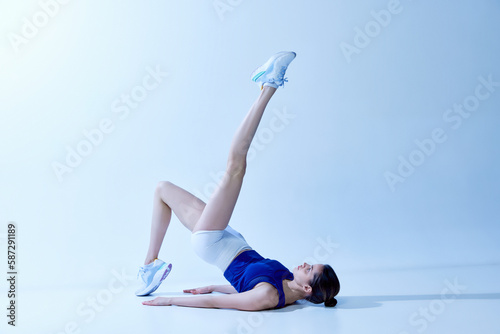 Portrait of young girl with fit sportive body training, doing stretching exercises against light blue studio background. Concept of sport, healthy and active lifestyle, beauty, fitness, wellness