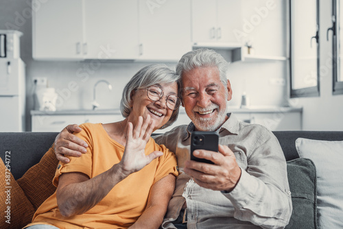 Happy retired family couple using mobile phone for video call together, talking to relations, getting good news, having fun, smiling and laughing. Carefree mature pensioners chatting online on cell.