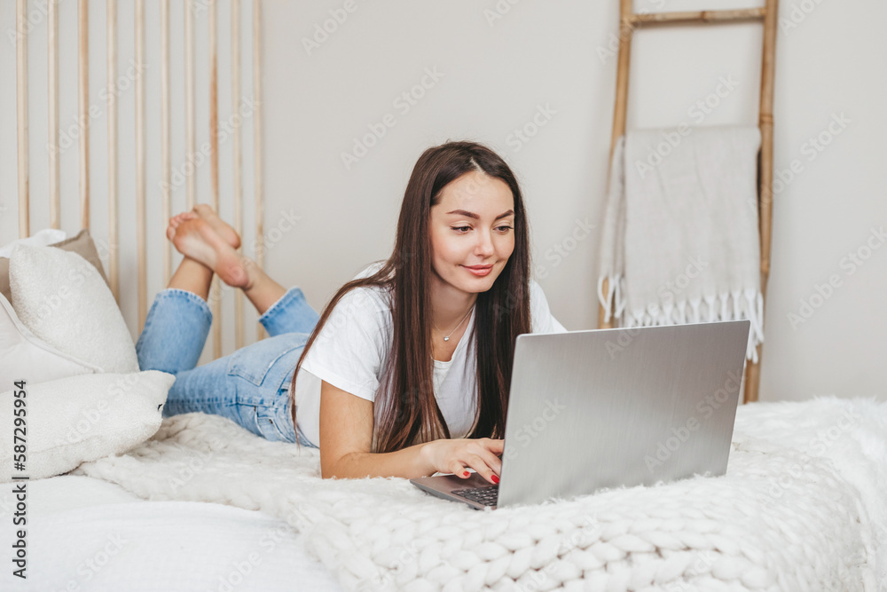 young woman lying on her stomach in bed work on laptop and takes online English courses young woman lying on her stomach in bed work on laptop and takes online English courses