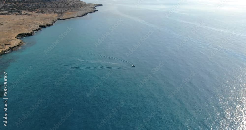 The copter flight over the steep shore of island and the deep blue sea and a small yacht or boat sailing on water in Cyprus. The copter flight over the steep shore of island and the deep blue sea and a small yacht or boat sailing on water in Cyprus.