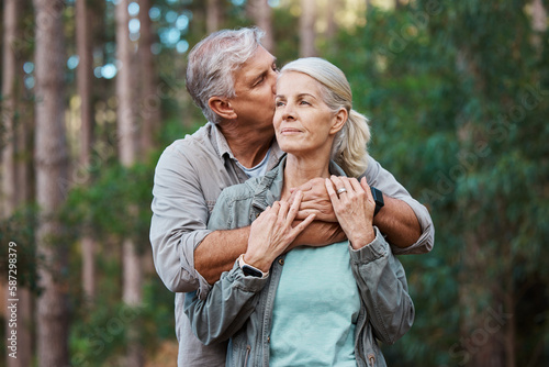 Hiking  kiss and senior couple with love in a forest  relax and hug while standing in nature park together. Caring  embrace and sweet  elderly man with woman on retirement vacation in the woods