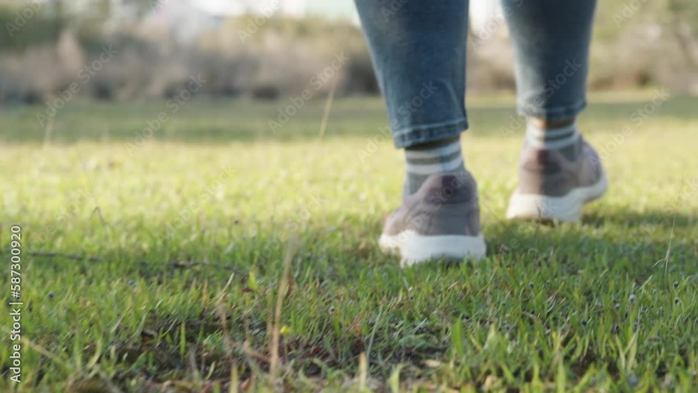 A woman in sneakers and jeans walks on the green grass in the forest, A close-up view from below. A woman in sneakers and jeans walks on the green grass in the forest, A close-up view from below.