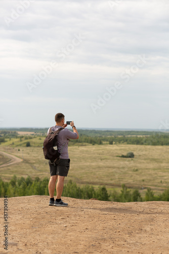 A man stands on a hill and takes pictures of the view on his phone