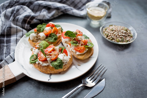 Bruschetta (sandwiches) with cherry tomatoes, mozzarella cheese and herbs on a stylish plate on a dark background. A traditional Italian snack.