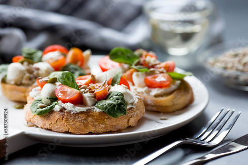Bruschetta (sandwiches) with cherry tomatoes, mozzarella cheese and herbs on a stylish plate on a dark background. A traditional Italian snack.
