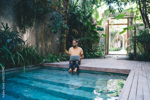 Man sitting on poolside with laptop and smartphone