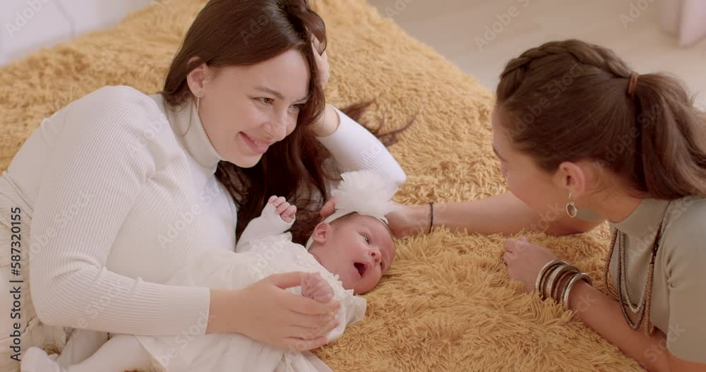 Two young women look at a newborn, talking, smiling. Baby's first days