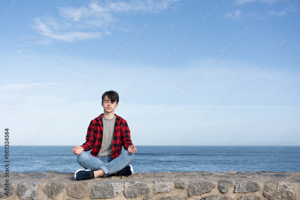 Teenager boy meditating outdoors at the coast
