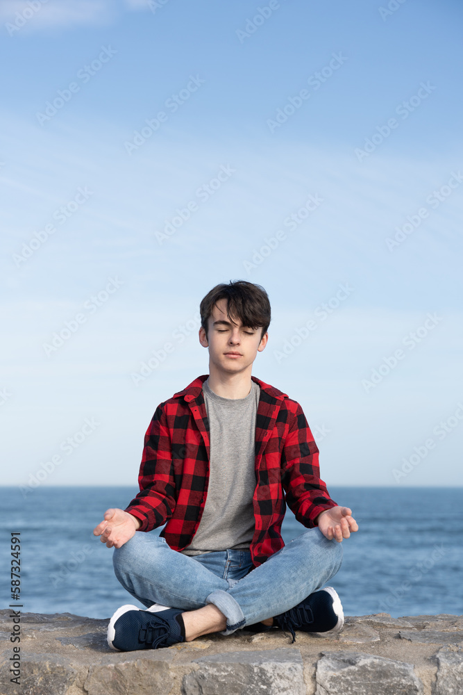 Teenager boy sitting in lotus pose outdoors