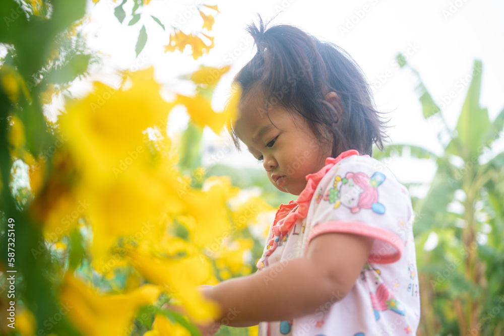Beautiful asian toddler girl playing with yelow flower outdoor park