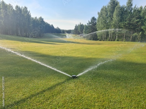 Sprinklers watering system working in fairway and sand bunker of green golf course