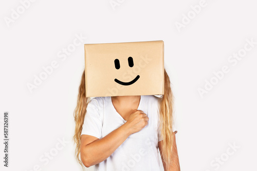 Mujer sonriente con una caja de cartón en la cabeza y con la mano en el corazón uuuuuun fondo blanco liso y aislado. Vista de frente y de cerca. Copy space