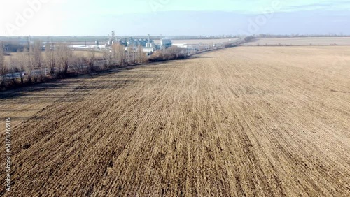 Agricultural industrial landscape. Plowed field after harvesting dry wheat, an elevator, a highway with moving cars on an autumn sunny day. Yellow field with dug up earth, road, cars, grain elevator