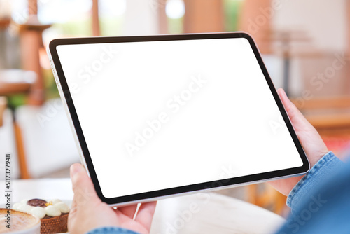 Mockup image of a woman holding digital tablet with blank white desktop screen with cake and coffee cup on the table in cafe