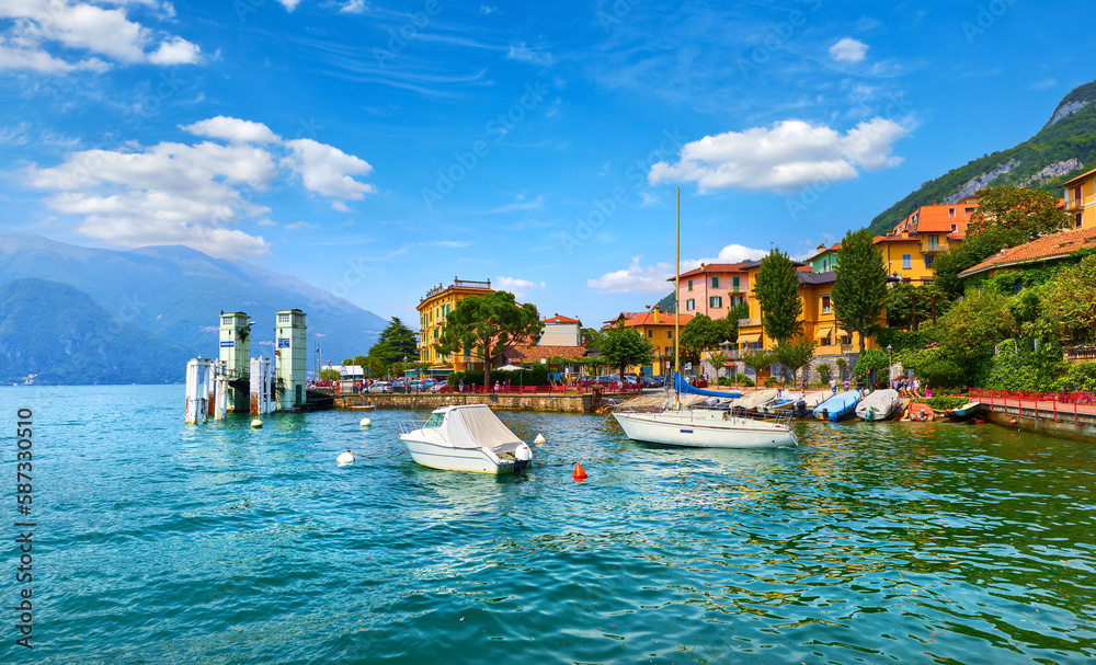 Varenna, Italy. Picturesque town at lake Como. Colourful motley Mediterranean houses stone beach coastline among green trees. Popular luxury health resort and touristic location. Summer day landscape