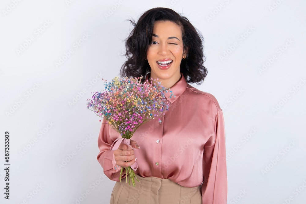 Coquettish young woman holds big bouquet of nice flowers over white background smiling happily, blinking at camera in a playful manner, flirting with you. Coquettish young woman holds big bouquet of nice flowers over white background smiling happily, blinking at camera in a playful manner, flirting with you.