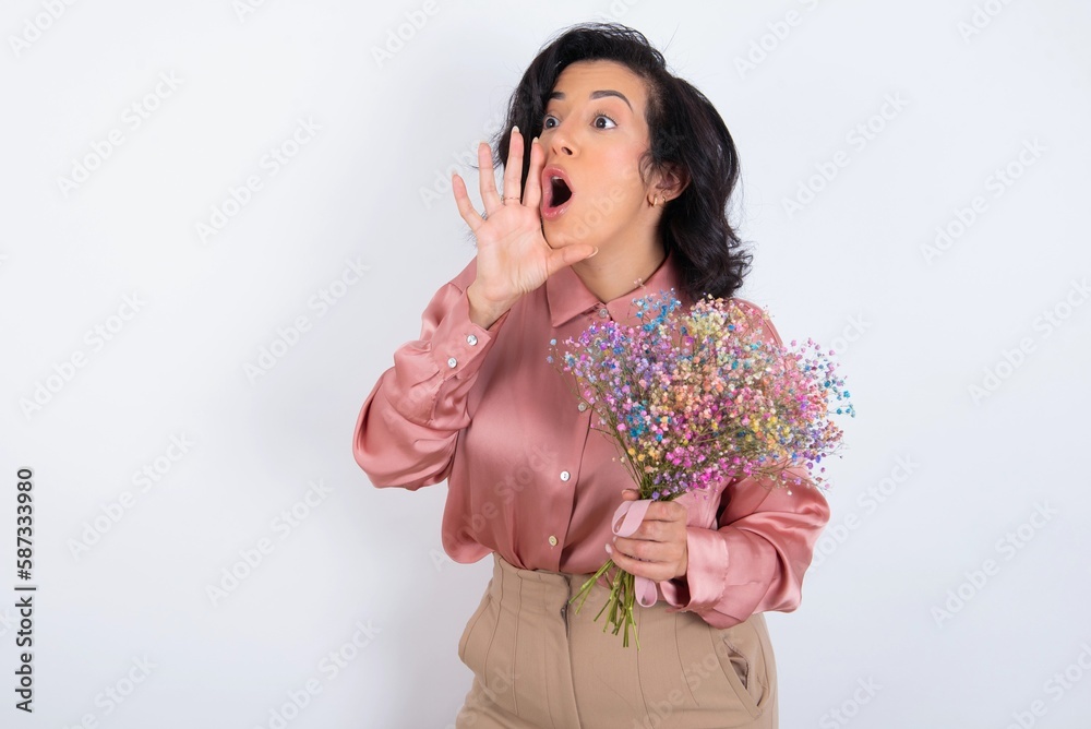 young woman holds big bouquet of nice flowers over white background shouting and screaming loud to side with hand on mouth. Communication concept. young woman holds big bouquet of nice flowers over white background shouting and screaming loud to side with hand on mouth. Communication concept.