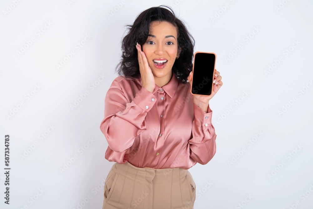 Naklejka premium young woman holds big bouquet of nice flowers over white background hold hand modern technology use touch face palm astonished impressed scream wow omg unbelievable unexpected