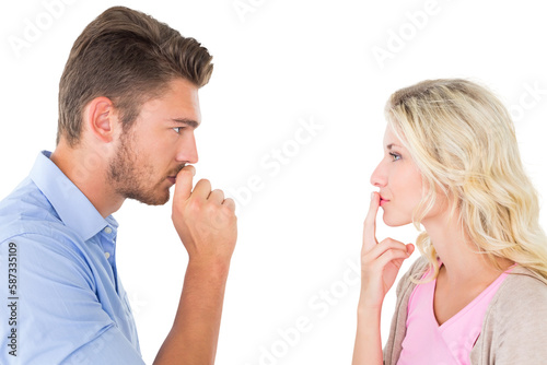 Young couple staying silent with fingers on lips