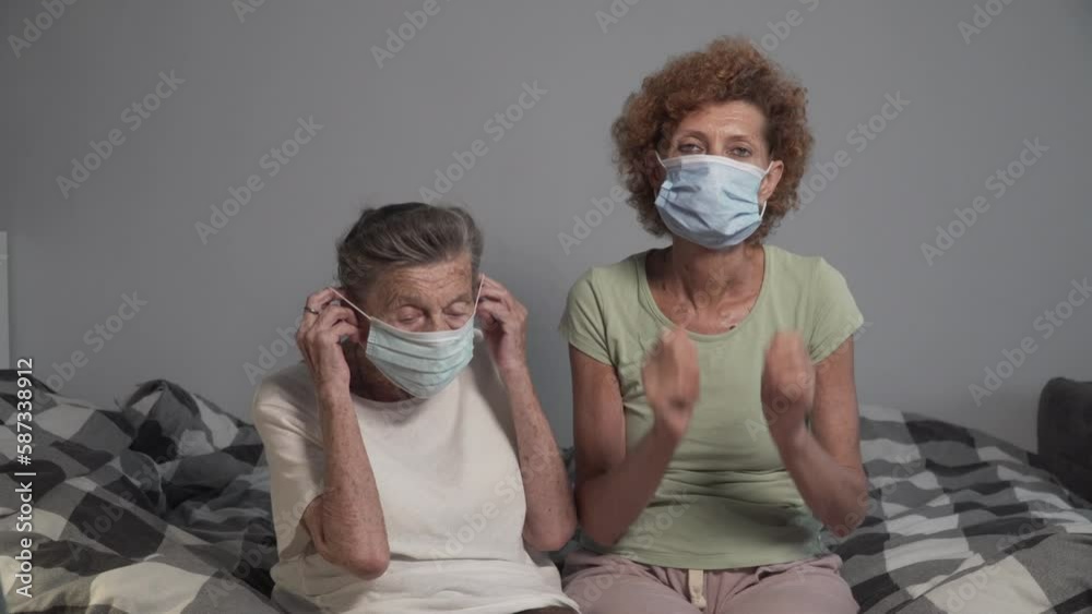 Two elderly women put on medical masks looking into camera sitting on