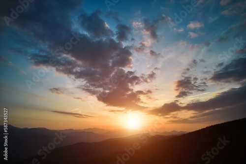 Panoramic view of bright evening sun and dramatic cloudy sky over mountains. Magnificent scenery of mountain hills under colorful evening sky with clouds and setting sun. Beauty of nature concept.