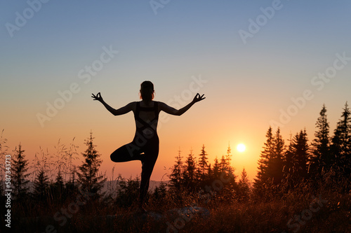 Sporty woman doing yoga exercises at early morning. Meditation with view of mountains. Silhouette of girl in gym suit practicing yoga poses.