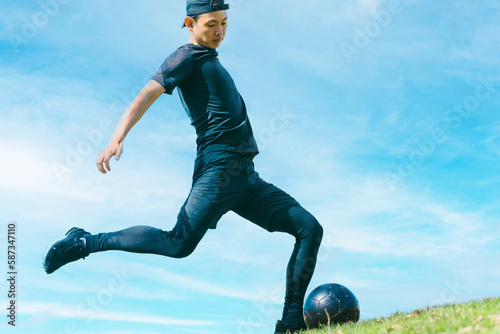 青空の下でサッカーボールを蹴る日本人男性 photo