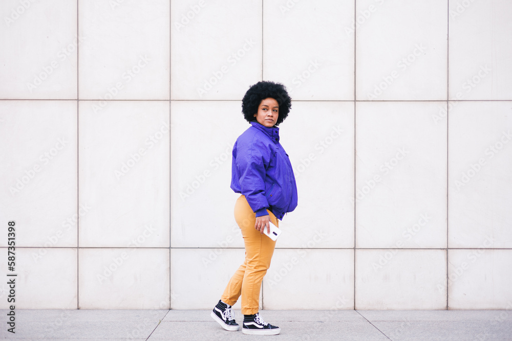 young latin afro woman standing on white wall using phone and smiling