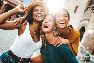 Three multiracial young women having fun walking on city street - Happy girlfriends hanging outside on a sunny day - Different females laughing together outside - Life style and friendship concept