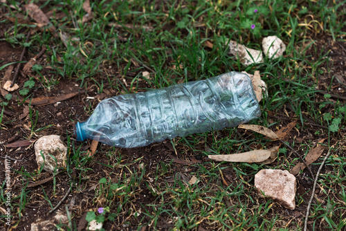 Abandoned garbage waste on nature. Environmental damage caused by human garbage pollution. Left plastic bottle among the grass on the river bank