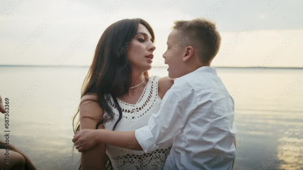 a happy young family of four has fun by the pond on a bench, children have fun with their father and mother.
