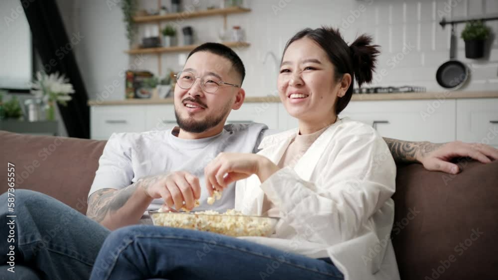 Couple watching TV Eating Popcorn Together. Korean family having fun sitting on couch at home. Happy wife and husband on sofa. Couple watching TV Eating Popcorn Together. Korean family having fun sitting on couch at home. Happy wife and husband on sofa.
