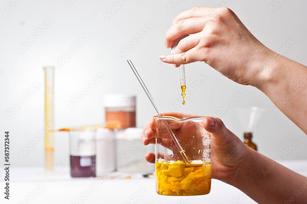 Dropping liquid from the dropper into a glass chemical vessel. Hands