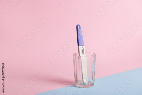 Still life. Inkjet pregnancy test with two bars, showing positive result in a transparent glass, isolated on a pink and blue pastel background. Finally pregnant. Quick Pregnancy Detection.